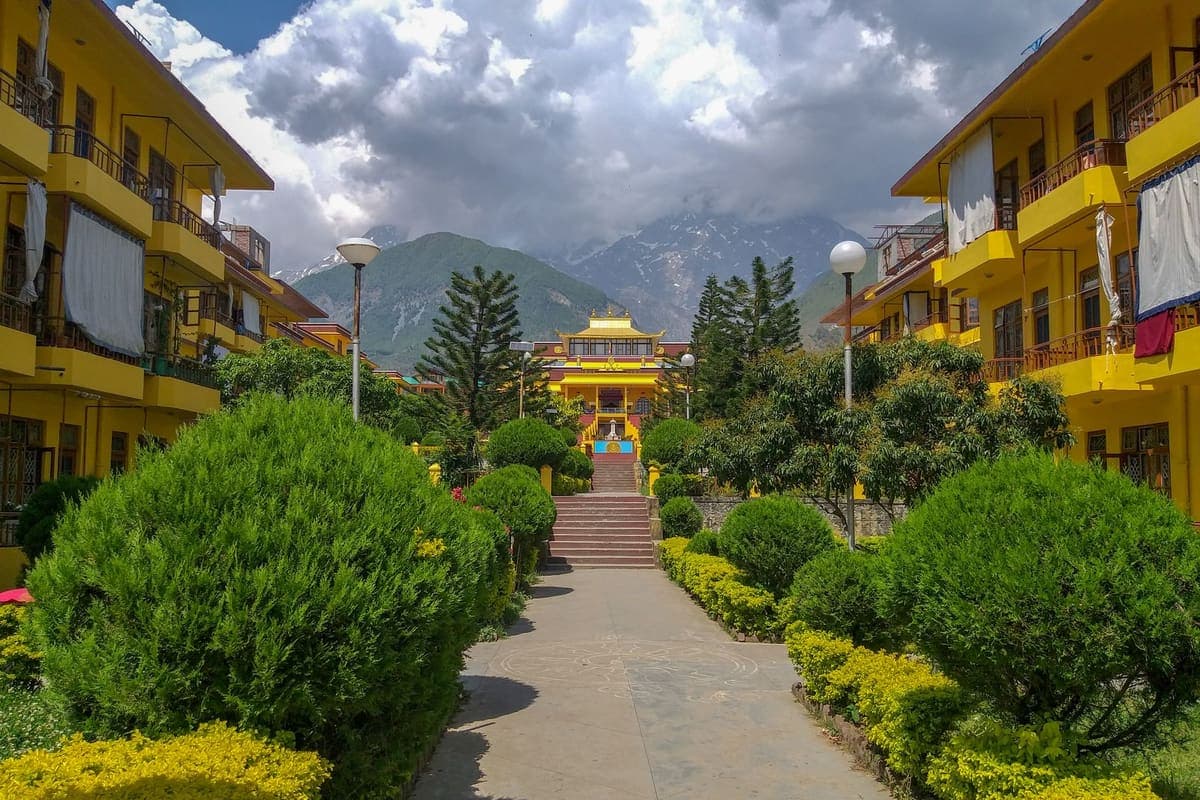 A brightly painted Buddhist monastery building set among green trees with mountains rising behind